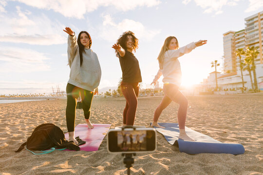 Women friends doing outdoor yoga on beach at sunrise