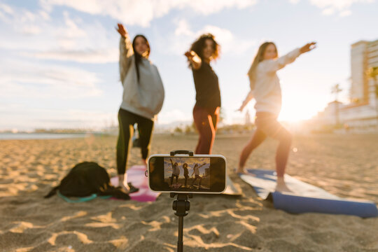 Women friends doing outdoor yoga on beach at sunrise