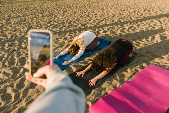 Women friends practise yoga on beach mats at sunrise