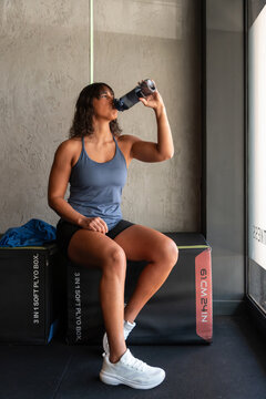 Woman drinking water after workout on gym plyo box