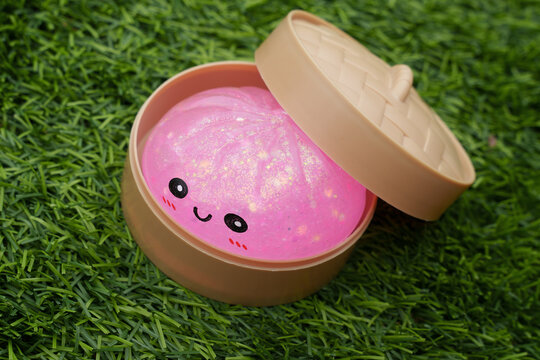 Cute pink glitter dumpling squishy in a small box placed on vibrant green grass, kawaii soft toy perfect for stress relief and play