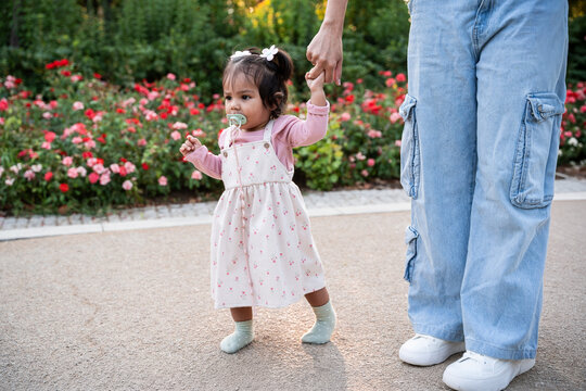 Mother holding baby daughter hand in garden walk