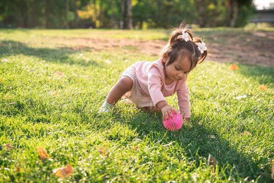 Latin baby girl playing on grass with pink spiky ball