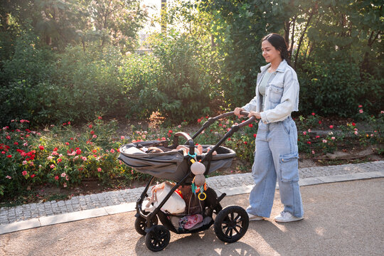 Latin mother pushing stroller with baby daughter in park
