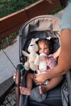 Latin mother feeding baby daughter in stroller outdoors