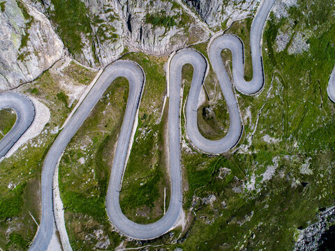 Aerial view of the historic Tremola road with its iconic serpentine hairpin turns and stone walls winding through the steep green mountain slopes near Airolo, Ticino, Switzerland.