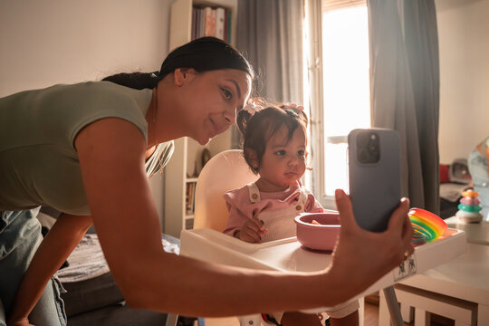 Latin mother taking a selfie with baby daughter at home