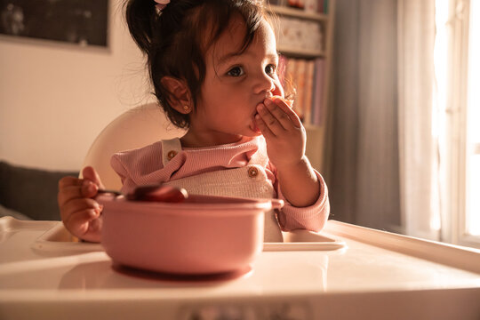 Latin baby girl eating breakfast in a sunlit kitchen