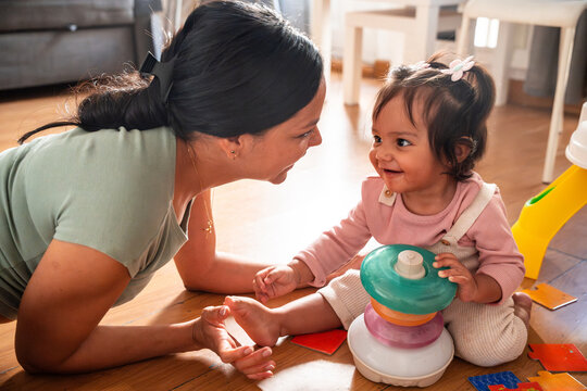 Latin mother and baby daughter playing at home on floor