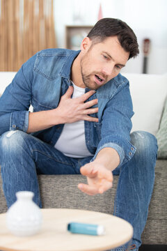 young man with asthma attack reaching for inhaler from table