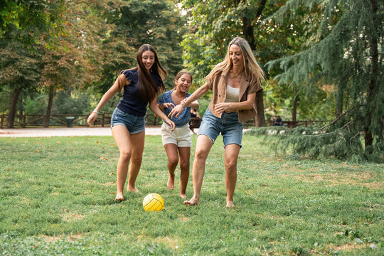 Mother and daughters playing soccer barefoot in summer park