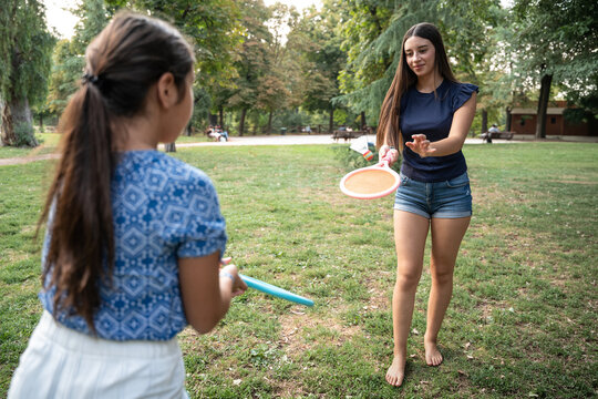 Sisters playing paddle ball game on grassy park lawn