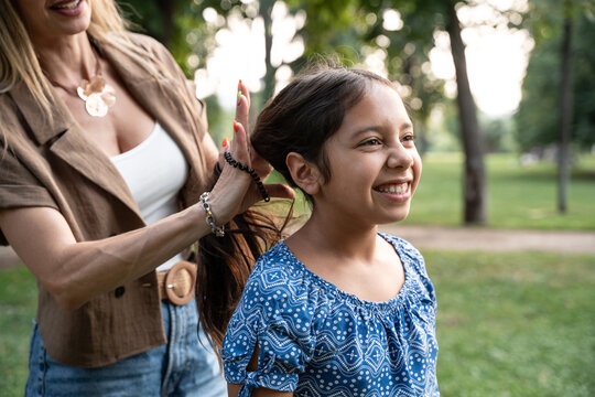 Mother styling daughter hair in park during sunny day