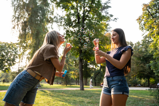 Mother and daughter blowing bubbles together in summer park