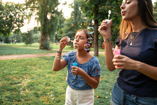 Sisters blowing soap bubbles together in a sunny park