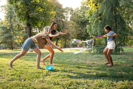 Family playing with giant soap bubble wand in summer park