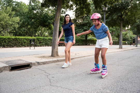 Two sisters rollerblading together in a park pathway