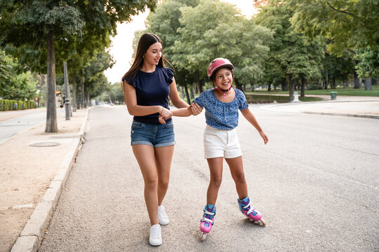 Older sister helps younger sister roller skate in park