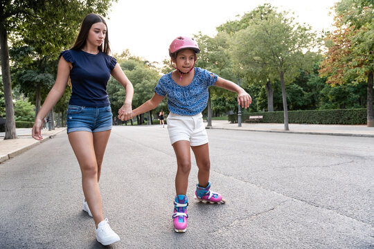 Older sister helping girl learn inline skating in park