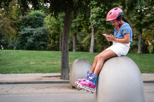 Girl with helmet using smartphone while wearing rollerblades
