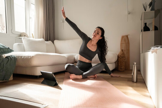 Woman doing yoga stretch at home with tablet workout