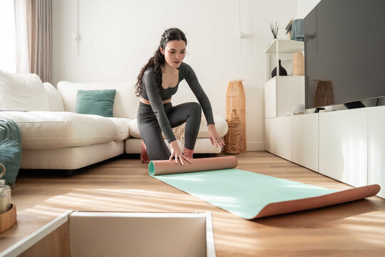 Woman unrolling yoga mat in bright modern living room