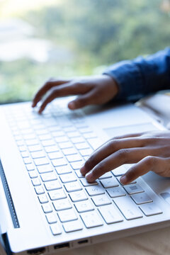 African American adult typing on white laptop keyboard with trackpad, USB-ports by window, in denim
