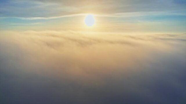 Sun rising above sea of thick clouds in blue morning sky aerial view flying through fluffy mist clip.