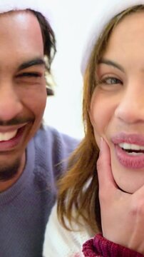 Vertical video: Starting selfie, couple in Santa hats squeezing cheeks and celebrating at home