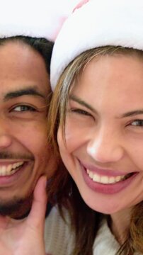 Vertical video: Selfie cam starting couple fixing Santa hats laughing cupping chin, sweater at home