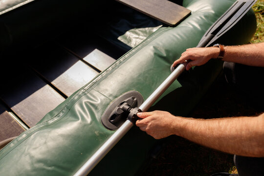 Close up of man hands installing aluminum oar in rowlock on board of green inflatable boat, fisherman assembly process of PVC watercraft, active summer weekend, outdoor recreation concept, copy space