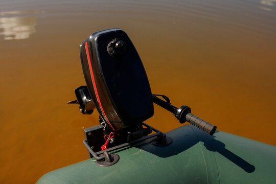 Black outboard engine motor installed on transom of green inflatable PVC boat in calm lake water, propeller detail close up, fisherman equipment preparation, active outdoor water recreation, copy spac