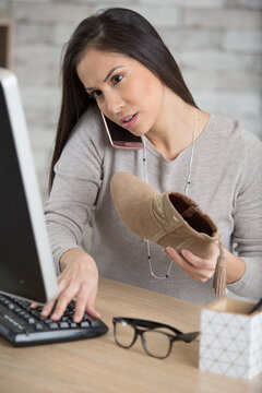 woman holding shoe and using computer and smartphone