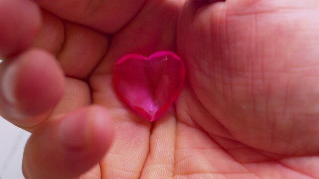 A small pink glass heart in a open palm.Close-up, natural light, cinematic.Perfect  simbol for romantic love, Valentine's Day, trust and tenderness.