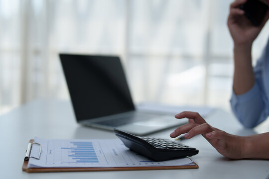 Person's hand actively using a calculator to crunch numbers for financial planning and accounting, working on reports with a laptop in a bright office environment