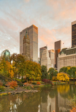 Manhattan skyscrapers and colorful autumn foliage reflect in a calm pond at sunset, representing urban tourism and seasonal travel in Central Park, Manhattan, New York City, USA.