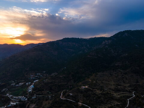 Aerial view of the lush Margalla Hills at sunset with winding roads and scattered buildings near Dino Valley Islamabad, Islamabad Capital Ter, Pakistan.