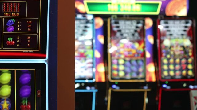 Blurred casino slot machines with colorful illuminated screens. Gambling, betting, gaming industry, luck, risk, entertainment, addiction and nightlife concept.