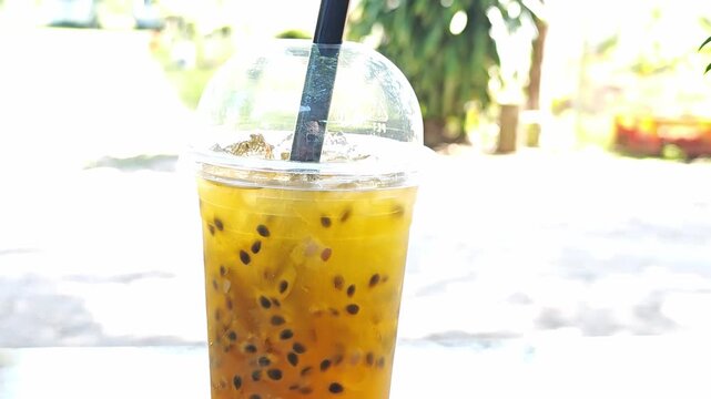 Iced passion fruit juice with pulp and seeds in a plastic cup.