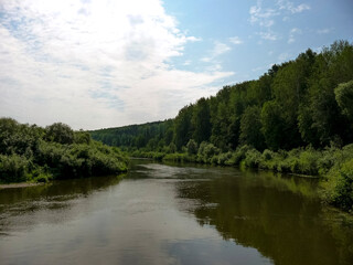 Obraz premium Serene river flowing through lush green forest landscape under blue sky 