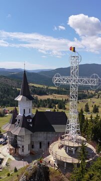 Aerial drone view of the large metal cross and Romanian flag near Acoperamantul Maicii Domnului Monastery in Dorna Arini. Vertical