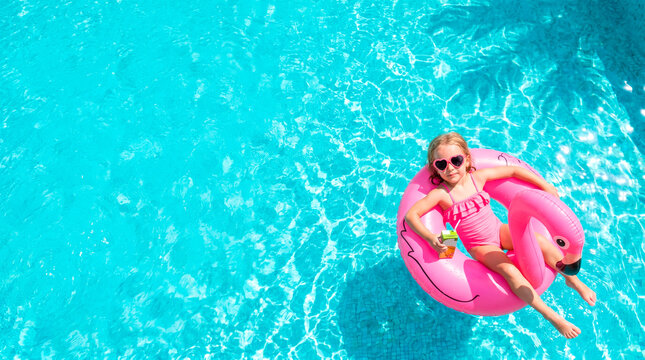 Little girl in pink swimsuit enjoys a summer day floating on a flamingo pool float