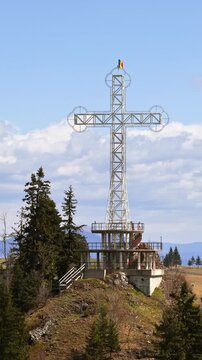 Aerial drone view of the large metal cross and Romanian flag near Acoperamantul Maicii Domnului Monastery in Dorna Arini. Vertical