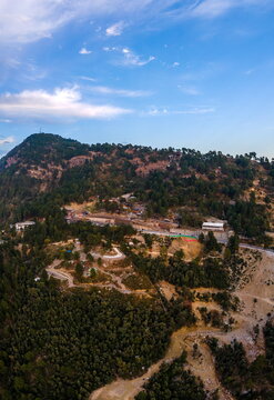 Aerial view of Dino Valley theme park nestled in the lush green Margalla Hills with winding roads and scattered buildings under a clear blue sky in Islamabad, Islamabad Capital Ter, Pakistan.