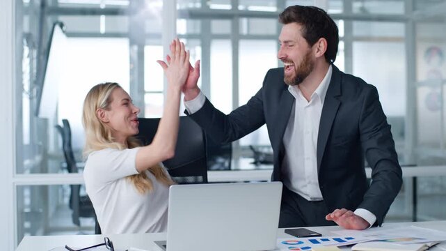 Business team two happy winners businesspeople workers winning with laptop giving high five in company Caucasian businesswoman with businessman win with computer celebrating smiling talking in office