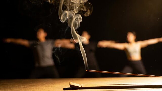 Lighting incense stick sending smoke in dark studio yoga class, group wearing sportswear breathing