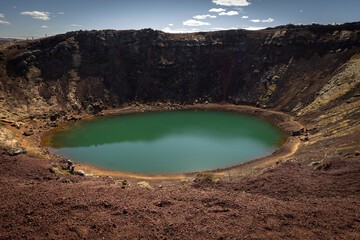 Un ancien cratère volcanique abrite un lac aux eaux vertes, entouré de parois rocheuses sombres et de sols volcaniques rouges. Cratère de Kerið, Cercle d'Or, Islande  © Tof - Photographie
