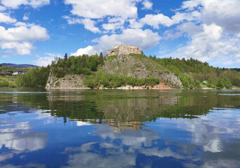 Fototapeta premium Ruins of Czorsztyn Castle on a rocky hill reflected in the calm water of Lake Czorsztyn, Pieniny, Poland. Medieval fortress under a blue sky on a sunny spring day. No people.