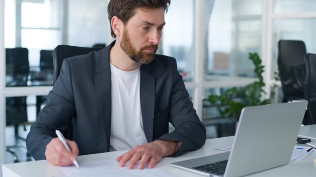 Concentrated Caucasian middle-aged business man signing contract typing laptop checking reports multitasking businessman male writing analyzing documents working computer multitask work in office
