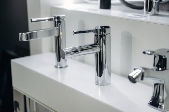 Modern chrome bathroom faucets displayed on a white countertop in a contemporary showroom, showcasing sleek designs and polished finishes for home improvement